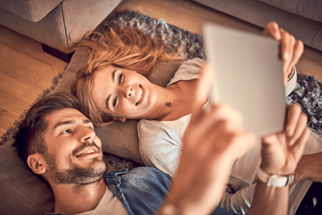 Ein Pärchen liegt auf dem Sofa und liest am Tablet